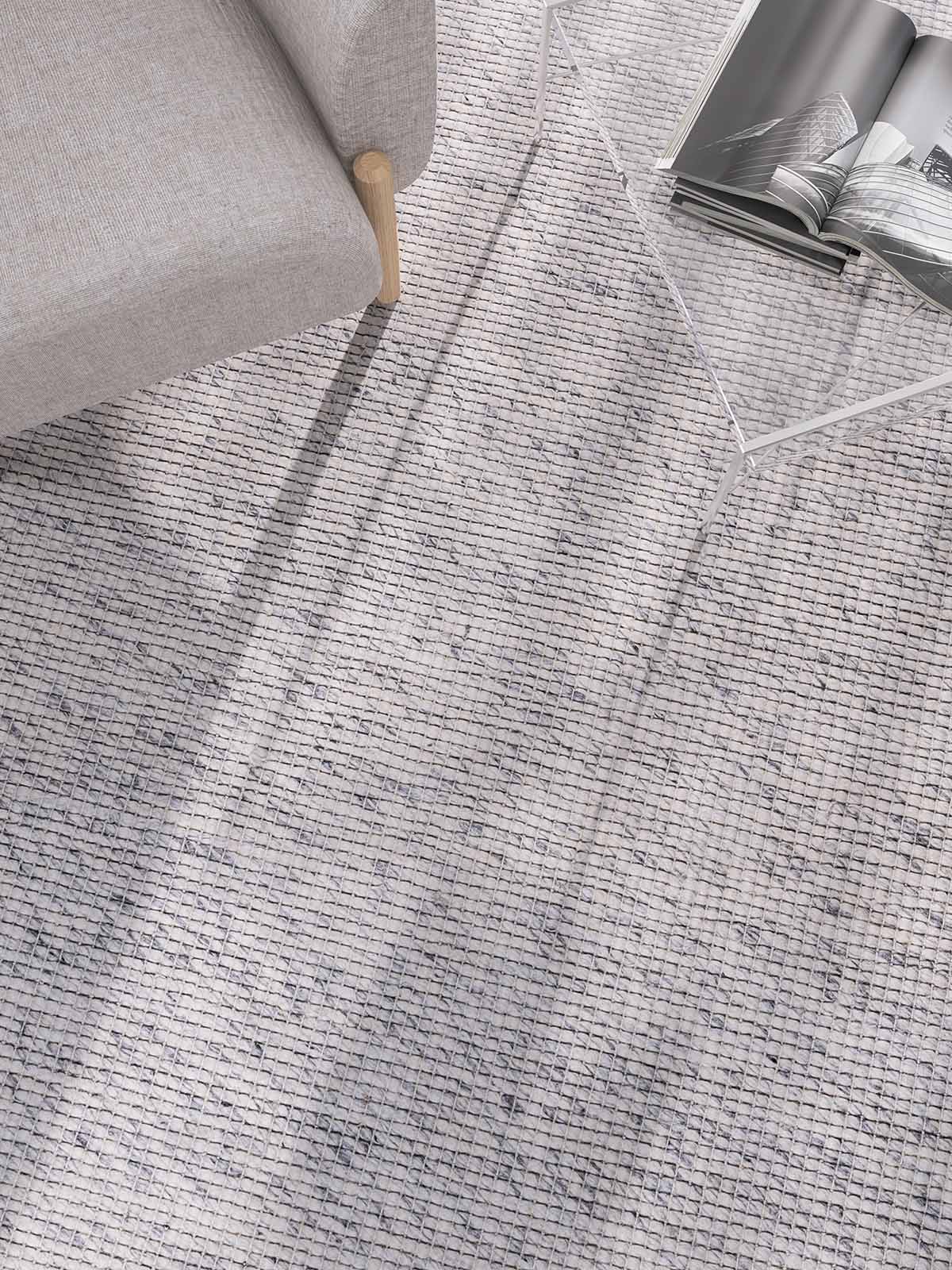 Large neutral premium Gray textured wool-cotton oscar alpine rug with a corner of a gray sofa and a glass table in the background