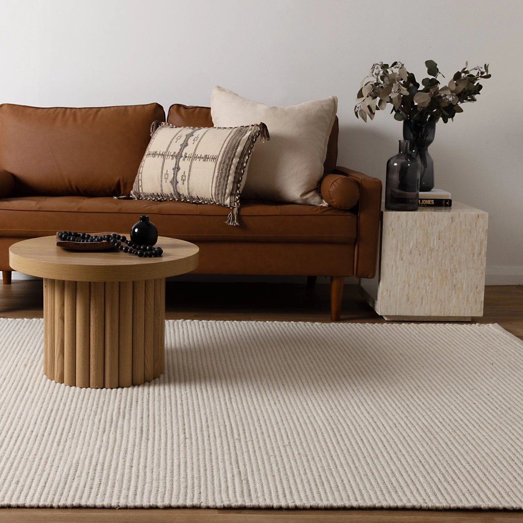 Brown leather sofa with decorative pillows in a living room, shows how fine the handwoven wool rug is in the ivory colour