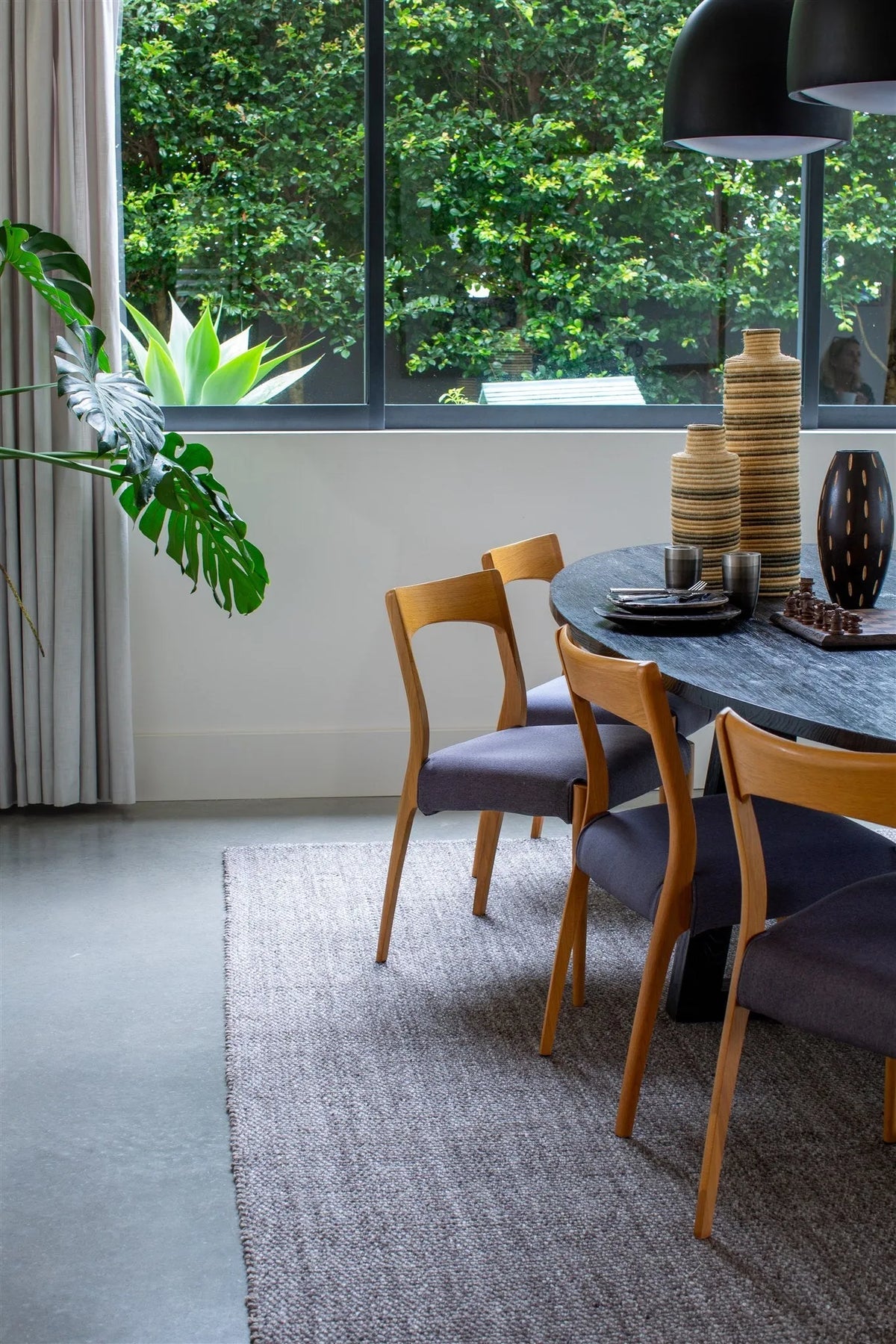 A premium handwoven wool rug is placed in a Dining area with a table and chairs near a large window with greenery outside forest sort of vibe on the backgroud. natural-looking style interior