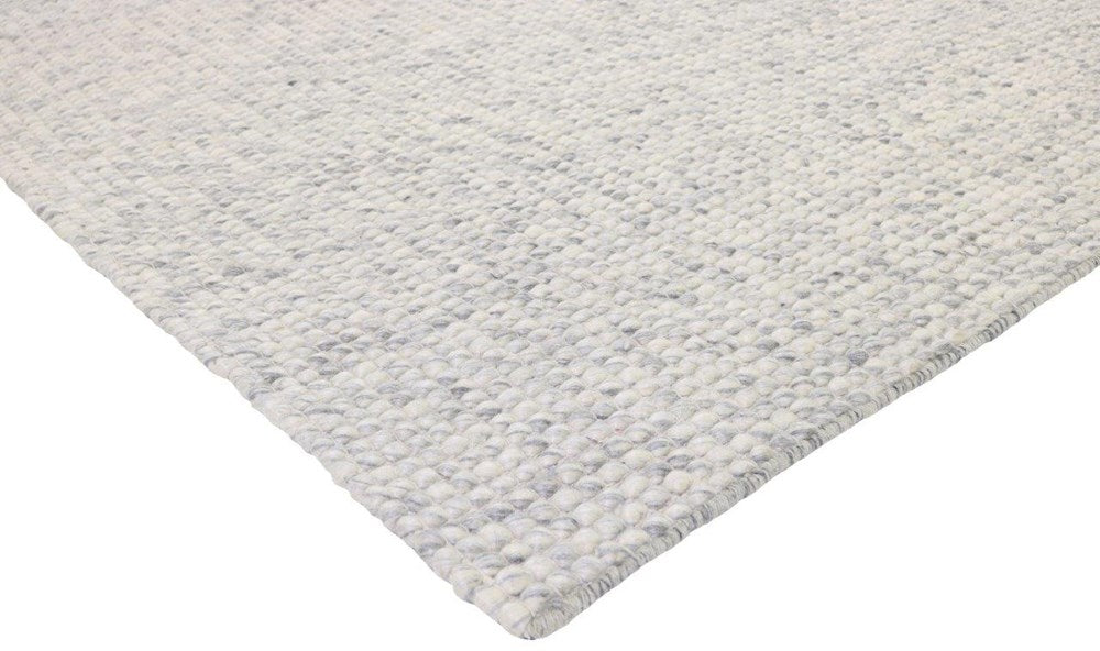Close-up of a textured light grey wool gray rug corner on a white background